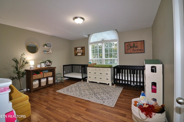 bedroom featuring a nursery area and dark hardwood / wood-style flooring