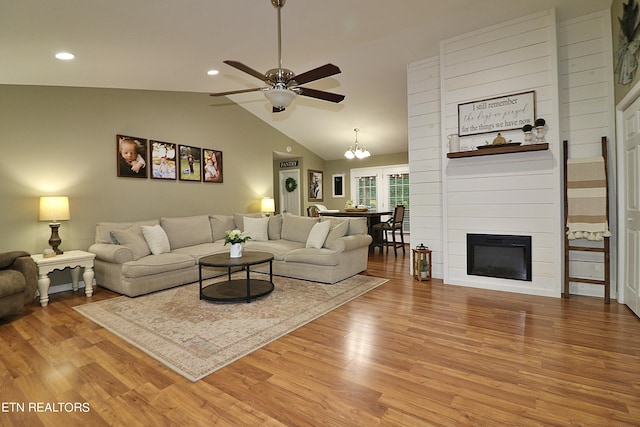 living room with ceiling fan with notable chandelier, lofted ceiling, a large fireplace, and hardwood / wood-style flooring