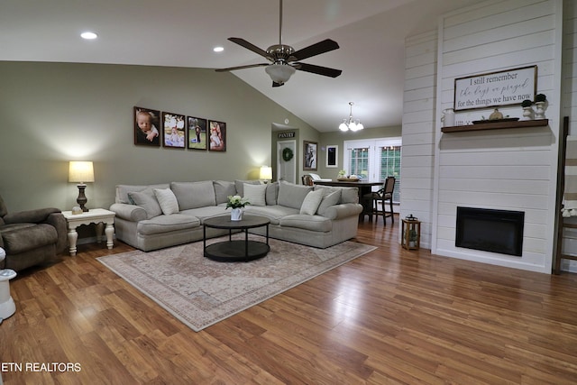 living room featuring ceiling fan with notable chandelier, lofted ceiling, hardwood / wood-style floors, and a large fireplace