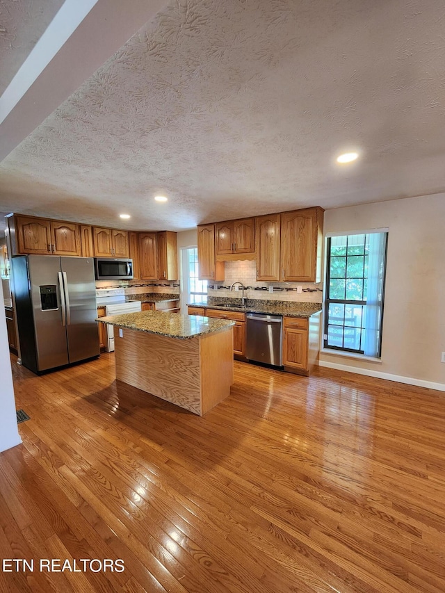 5725 Academy Dr, Morristown, TN 37814 - kitchen featuring light stone counters, a kitchen island, stainless steel appliances, a textured ceiling, and light hardwood / wood-style flooring