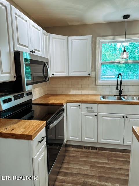 kitchen featuring appliances with stainless steel finishes, white cabinets, decorative light fixtures, wood counters, and sink