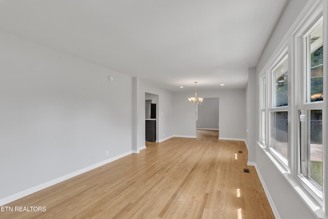 spare room featuring light hardwood / wood-style flooring, a chandelier, and a wealth of natural light