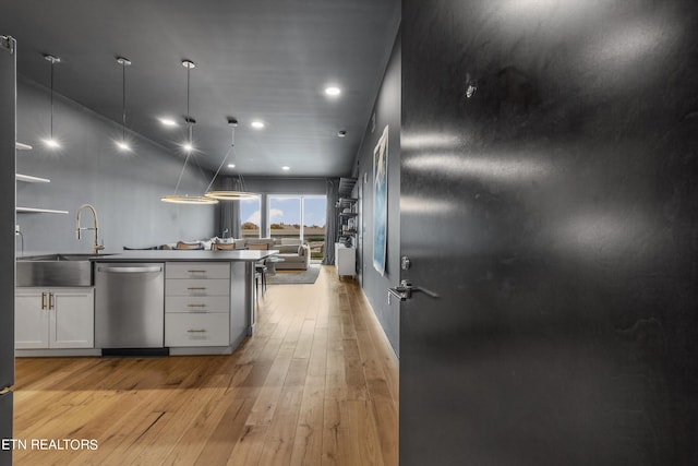 kitchen with pendant lighting, dishwasher, sink, white cabinetry, and light hardwood / wood-style flooring