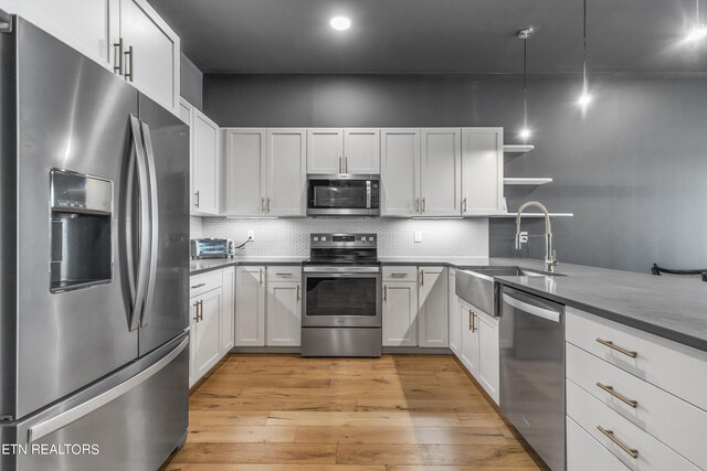 kitchen with white cabinets, pendant lighting, sink, stainless steel appliances, and light hardwood / wood-style floors