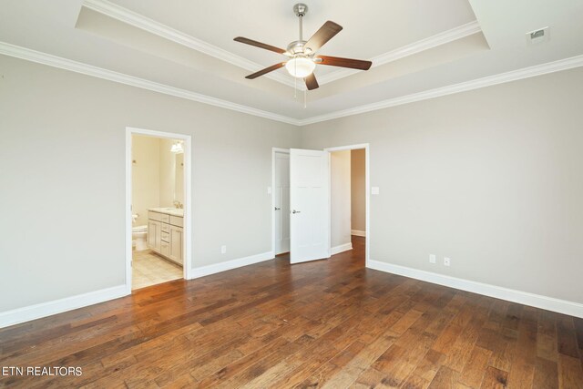 unfurnished bedroom featuring connected bathroom, ceiling fan, a tray ceiling, and dark wood-type flooring