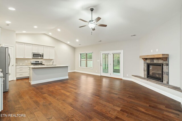 unfurnished living room featuring vaulted ceiling, ceiling fan, dark hardwood / wood-style floors, and a stone fireplace