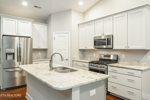 kitchen with white cabinets, appliances with stainless steel finishes, dark hardwood / wood-style flooring, and a kitchen island with sink