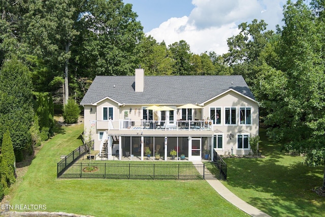 rear view of property featuring a balcony, a sunroom, and a lawn