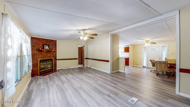 unfurnished living room featuring ceiling fan, vaulted ceiling with beams, light hardwood / wood-style flooring, and a brick fireplace