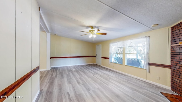 empty room with light wood-type flooring, ceiling fan, brick wall, and a textured ceiling