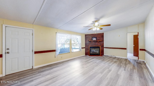 unfurnished living room with a brick fireplace, ceiling fan, light wood-type flooring, and a textured ceiling