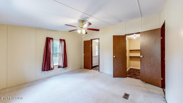 unfurnished bedroom featuring carpet floors, a spacious closet, ensuite bath, and ceiling fan