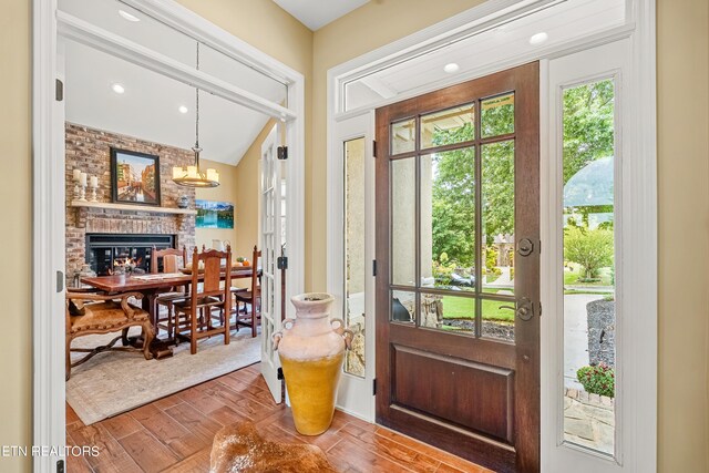 entrance foyer with wood-type flooring, a notable chandelier, lofted ceiling, and a fireplace