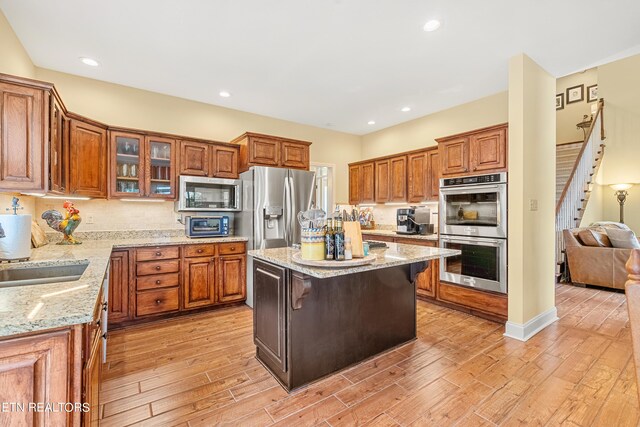 kitchen with light wood-type flooring, a kitchen island, stainless steel appliances, a breakfast bar area, and light stone countertops