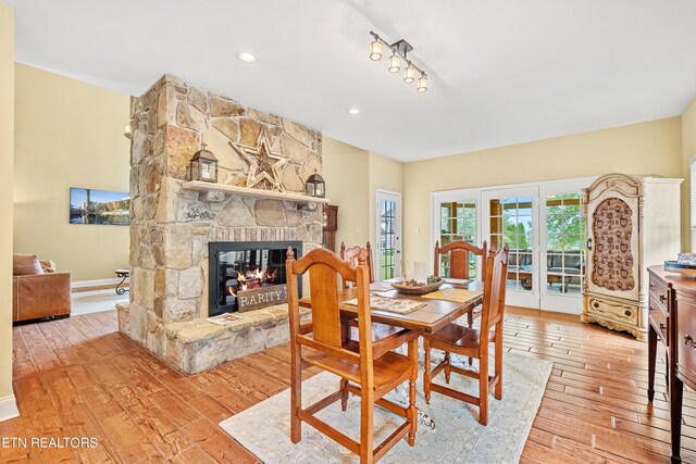 dining space featuring light wood-type flooring, french doors, and a stone fireplace