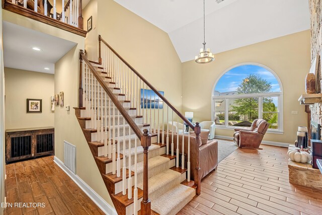 stairs featuring high vaulted ceiling, a chandelier, a fireplace, and hardwood / wood-style floors