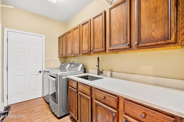 clothes washing area featuring cabinets, light hardwood / wood-style floors, washer and clothes dryer, and sink