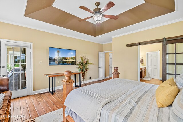 bedroom featuring ceiling fan, access to outside, light hardwood / wood-style flooring, a tray ceiling, and a barn door