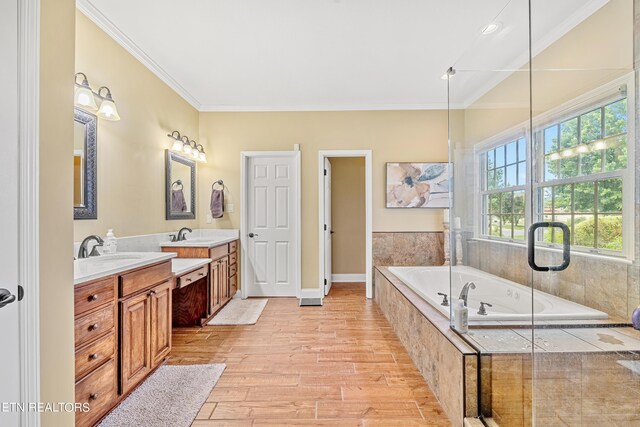 bathroom with wood-type flooring, vanity, ornamental molding, and a relaxing tiled tub