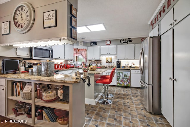 kitchen featuring a kitchen breakfast bar, a textured ceiling, white cabinetry, and stainless steel appliances