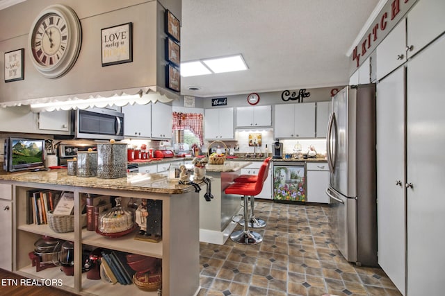 kitchen featuring a breakfast bar, stainless steel appliances, white cabinetry, and a textured ceiling