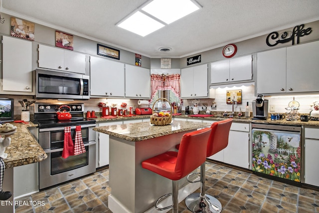 kitchen with light stone counters, white cabinets, appliances with stainless steel finishes, and a center island