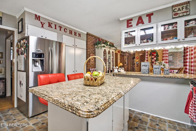 kitchen featuring white cabinets, a kitchen island, stainless steel refrigerator with ice dispenser, light stone countertops, and crown molding