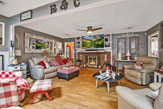 living room with light wood-type flooring, ceiling fan, and a fireplace