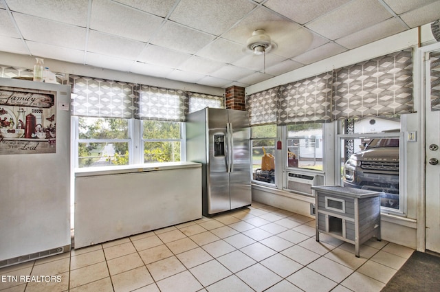 interior space with stainless steel refrigerator, a paneled ceiling, light tile patterned floors, ceiling fan, and stainless steel fridge