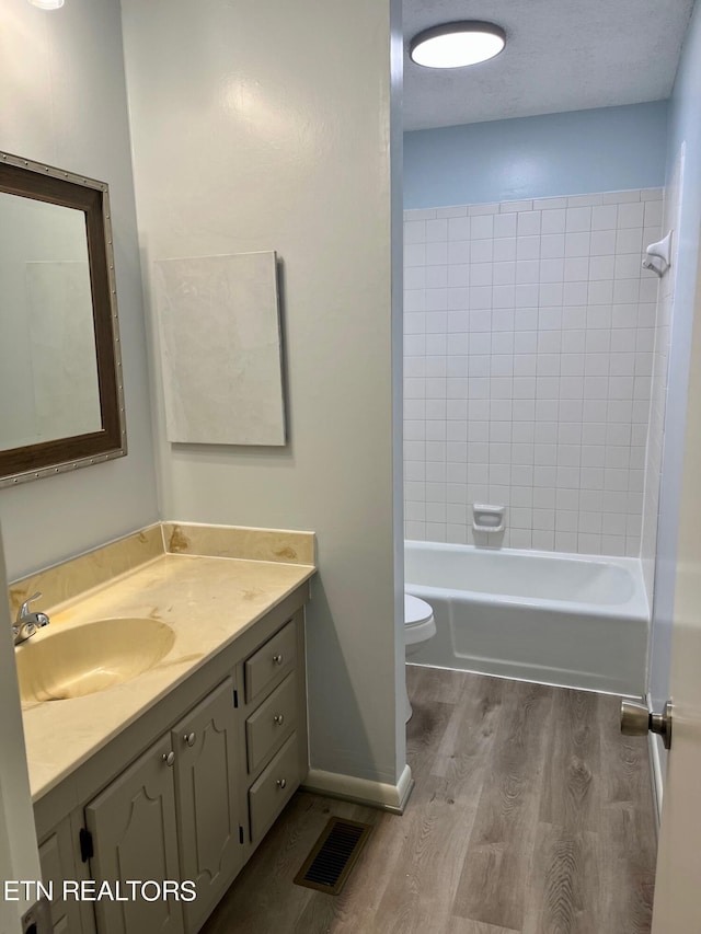 full bathroom with a textured ceiling, toilet, tiled shower / bath, vanity, and hardwood / wood-style flooring