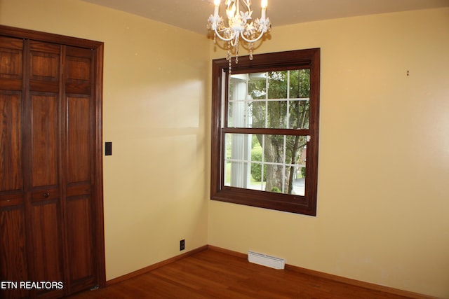 unfurnished room with dark wood finished floors, baseboards, and a chandelier