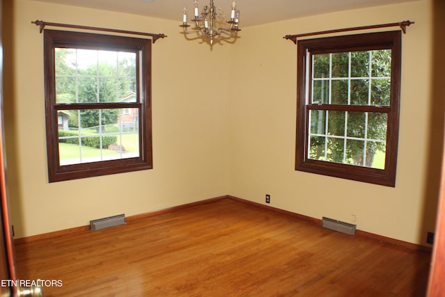 spare room featuring light wood finished floors, a healthy amount of sunlight, visible vents, and a chandelier