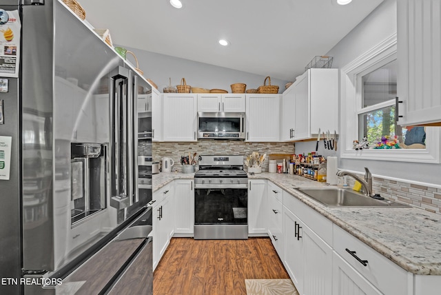 kitchen with appliances with stainless steel finishes, white cabinetry, vaulted ceiling, and sink