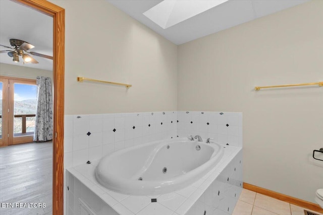 bathroom with tiled bath, a skylight, and ceiling fan