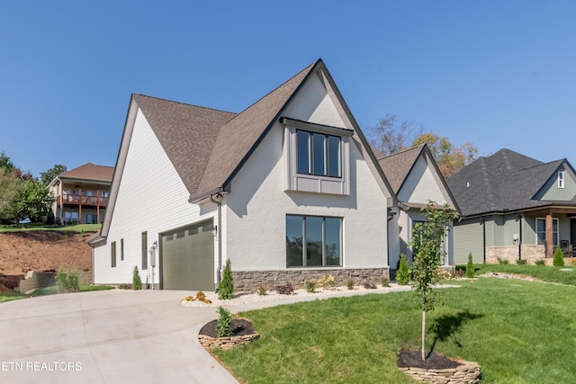 view of front of property with concrete driveway, a front yard, roof with shingles, stone siding, and an attached garage