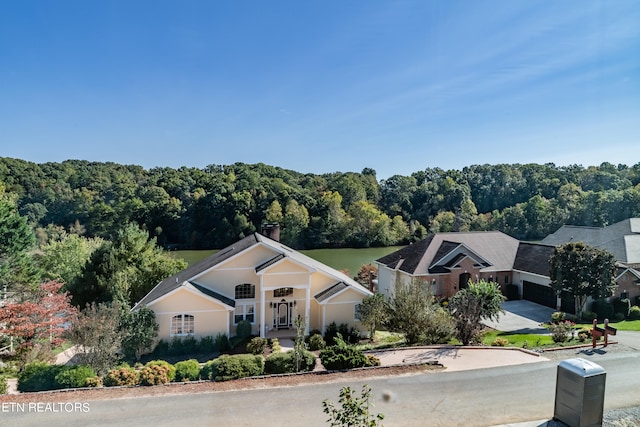 view of front of house with a chimney, an attached garage, concrete driveway, and a forest view