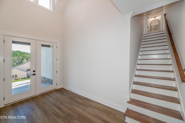 staircase featuring french doors, a high ceiling, baseboards, and wood finished floors