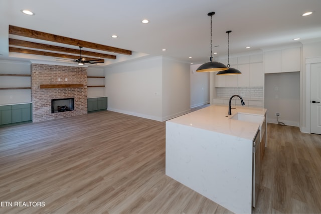 kitchen featuring beamed ceiling, a sink, decorative backsplash, white cabinets, and a brick fireplace