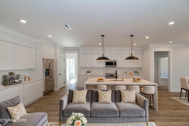 living room featuring light wood-type flooring, visible vents, ornamental molding, and recessed lighting