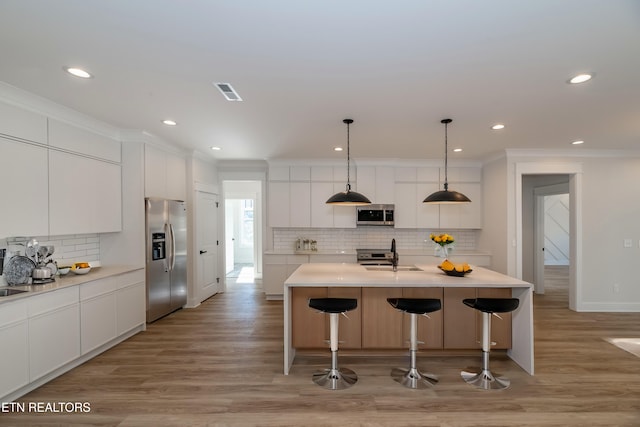 kitchen featuring visible vents, ornamental molding, stainless steel appliances, light wood-style floors, and modern cabinets