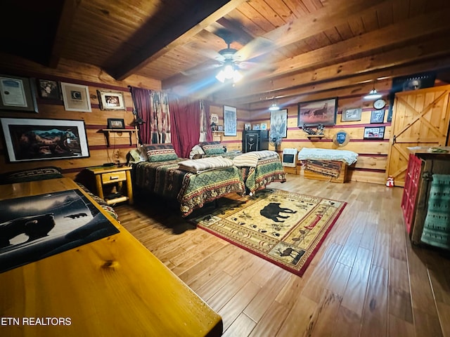 bedroom with hardwood / wood-style flooring, beam ceiling, wood walls, a barn door, and wooden ceiling