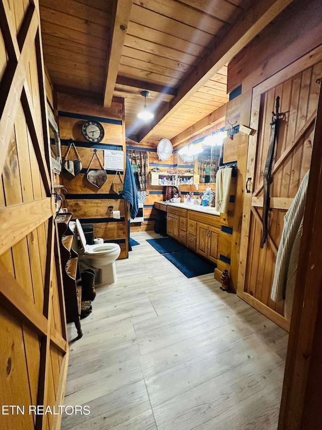 interior space with toilet, beam ceiling, wooden walls, a workshop area, and hardwood / wood-style floors