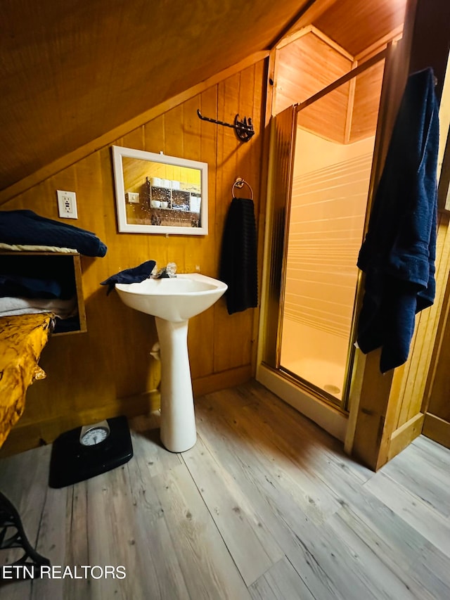 bathroom featuring wooden walls, hardwood / wood-style floors, vaulted ceiling, and an enclosed shower