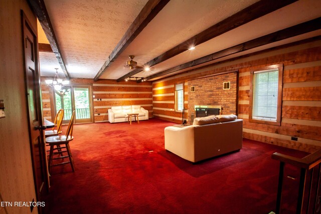 living room featuring carpet floors, ceiling fan with notable chandelier, a fireplace, and beamed ceiling