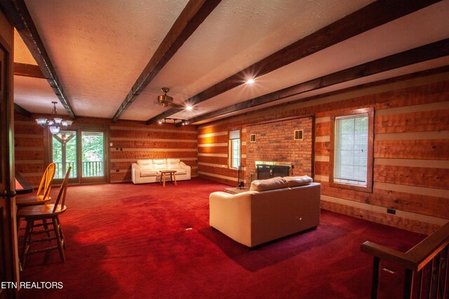 carpeted living room with ceiling fan with notable chandelier, wood walls, beamed ceiling, and a brick fireplace