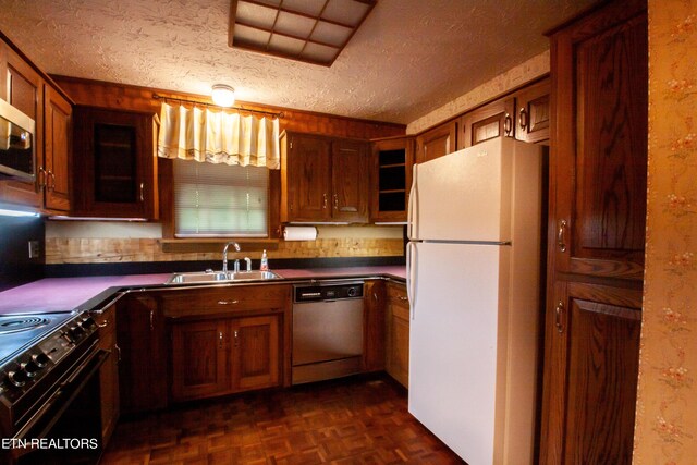 kitchen with dishwasher, white refrigerator, a textured ceiling, sink, and black range oven