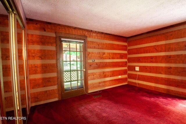 carpeted empty room featuring wooden walls and a textured ceiling