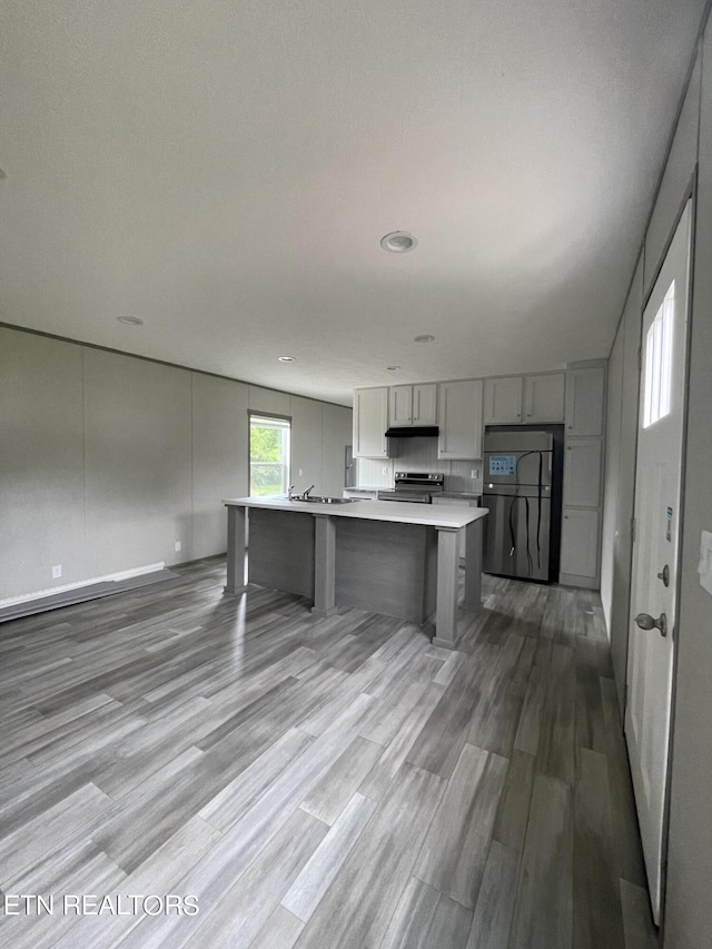 kitchen featuring a kitchen island with sink, gray cabinets, stainless steel appliances, light wood-type flooring, and a kitchen bar