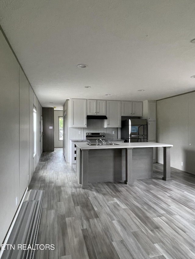 kitchen with an island with sink, gray cabinetry, a textured ceiling, light hardwood / wood-style flooring, and refrigerator