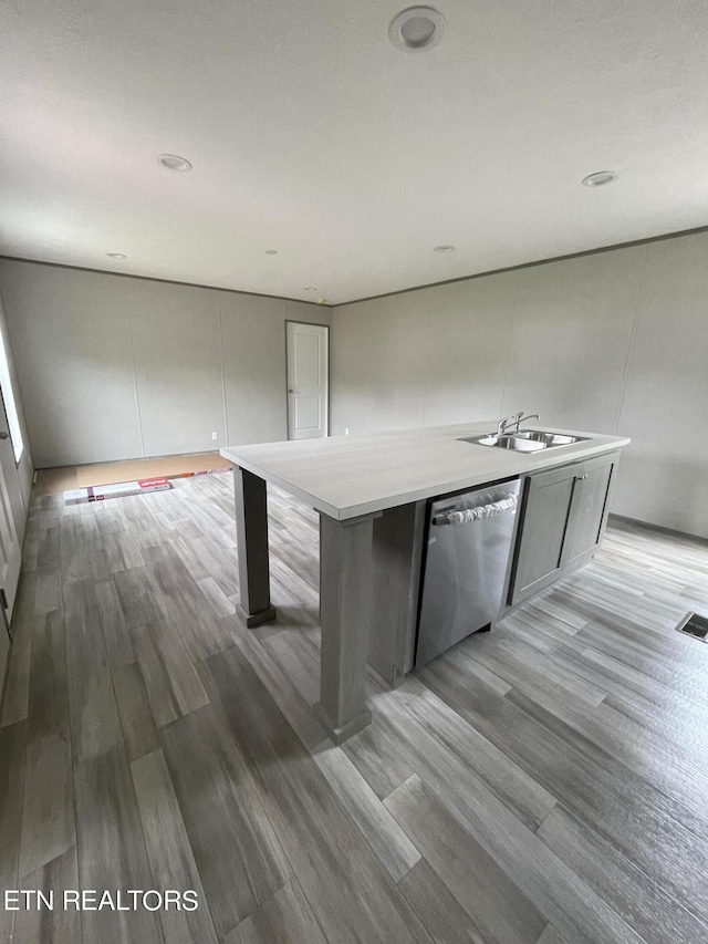 kitchen with a spacious island, dishwasher, sink, and light hardwood / wood-style floors